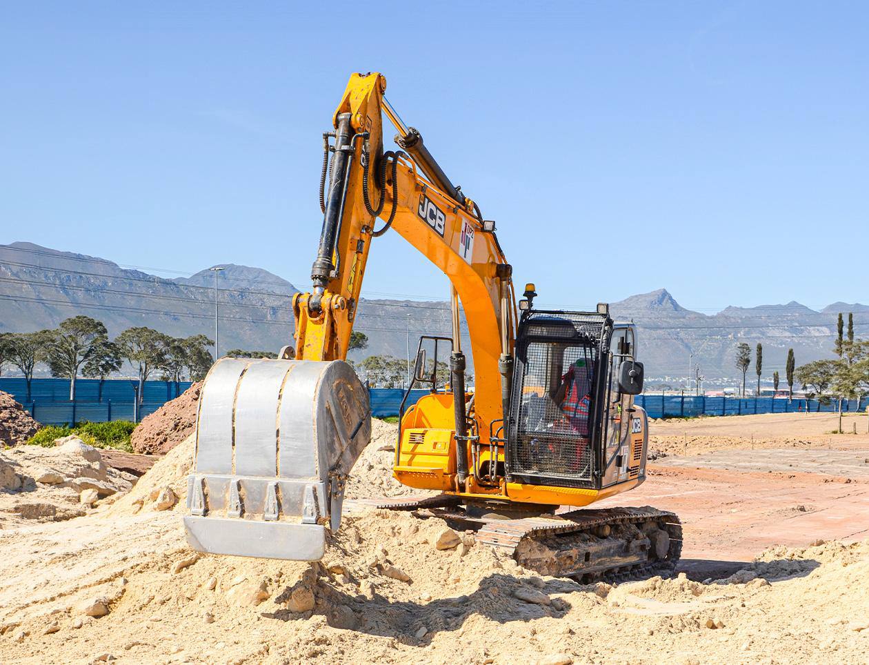Tracked excavator working on a sand sub-base with mountains behind.