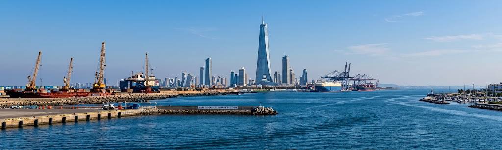 Port with cargo cranes and container ships in front of a city skyline.